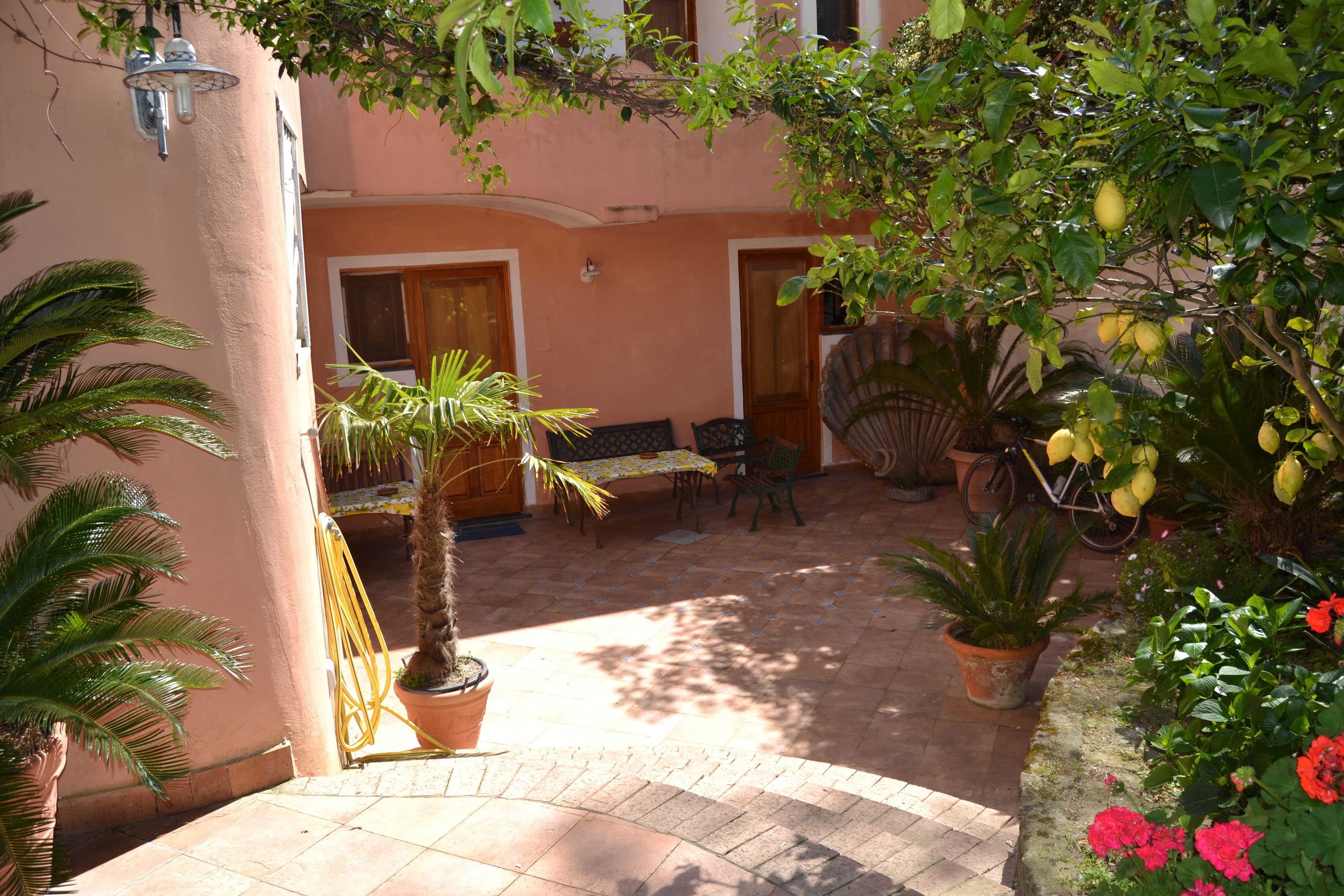 A courtyard with a tiled floor, a table and chairs, potted plants, and a bicycle.