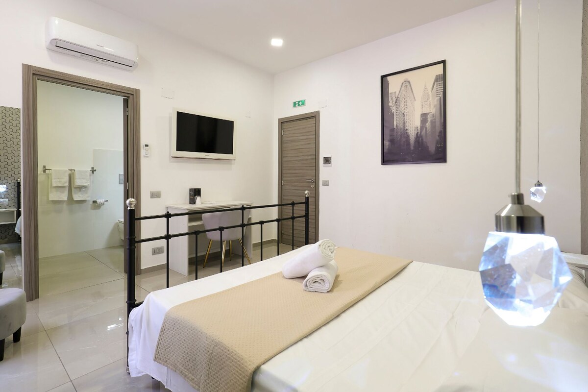Ein Hotelzimmer mit Bett, Schreibtisch, Stuhl, Fernseher und einem durchgegangenen Tür sichtbaren Badezimmer.