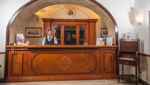 A reception desk with a wooden finish, a framed picture on the wall, and a small desk with a lamp to the right. - Hotel La Pace (Naples)