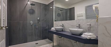 Un baño moderno con ducha a ras de suelo, tocador con dos lavamanos y secador de pelo montado en la pared.