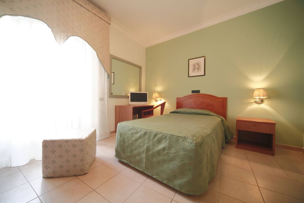Una camera da letto con un letto, una scrivania, una sedia, un comodino e una lampada.