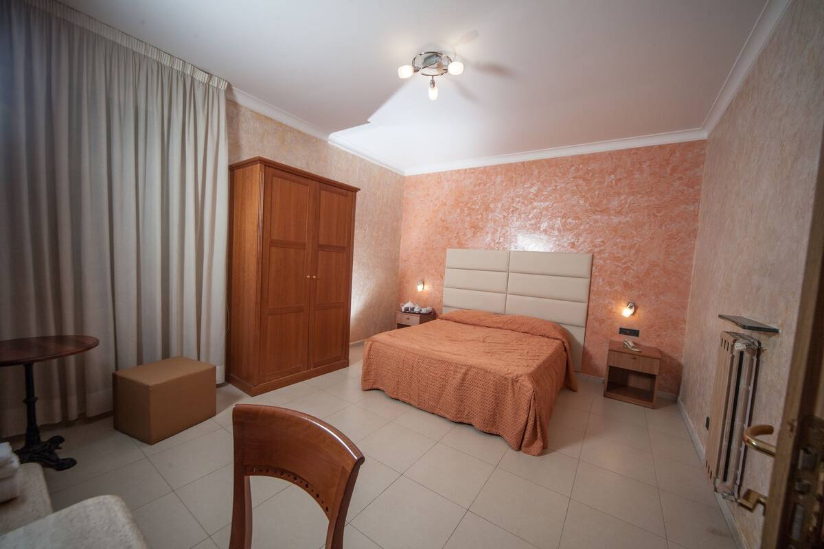 Una camera da letto con un letto, comodini, un armadio, una sedia e un piccolo tavolo.