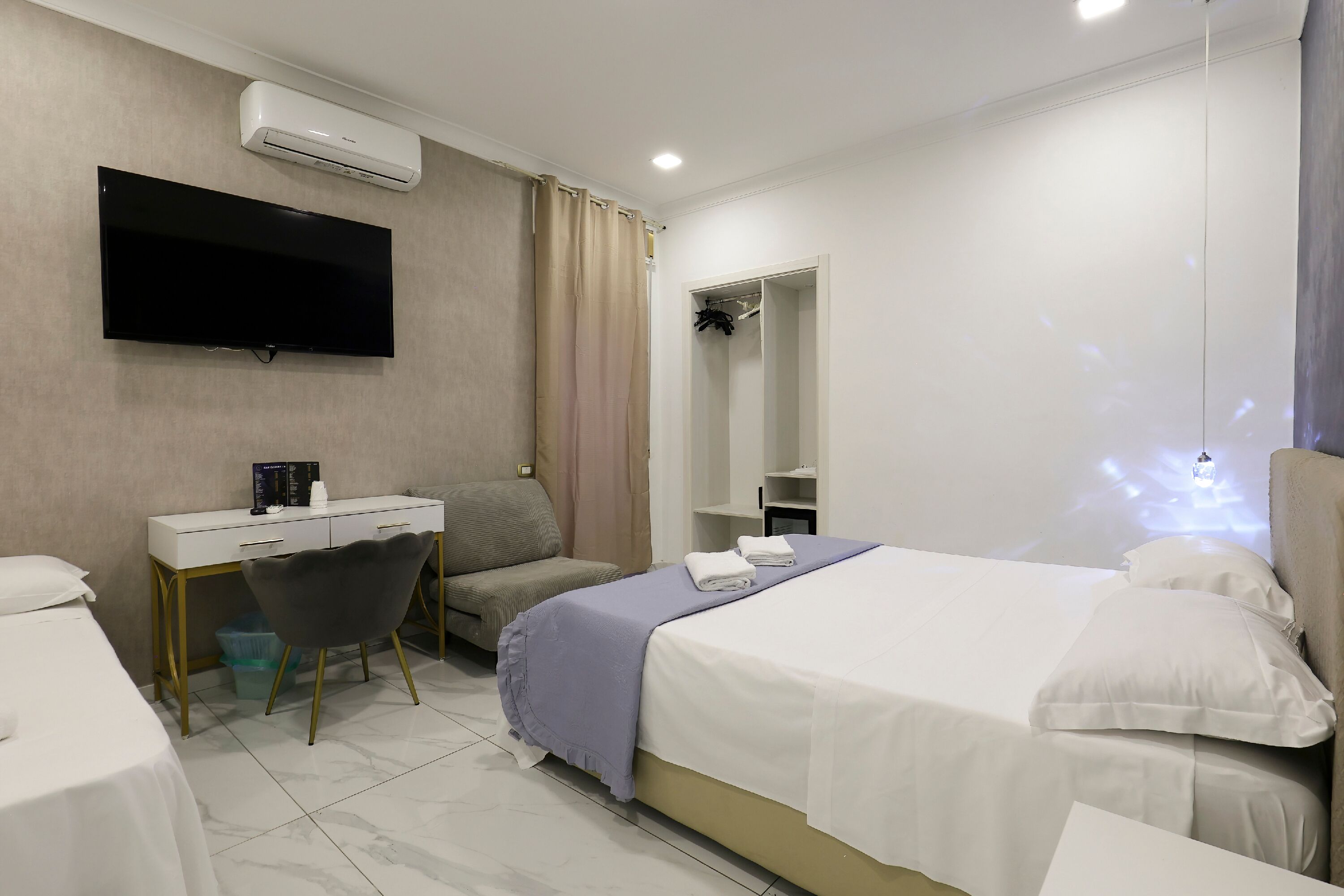 A modern hotel room with a bed, a desk, a chair, a TV, and a wardrobe.