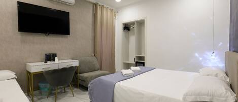 A modern hotel room with a bed, a desk, a chair, a TV, and a wardrobe.