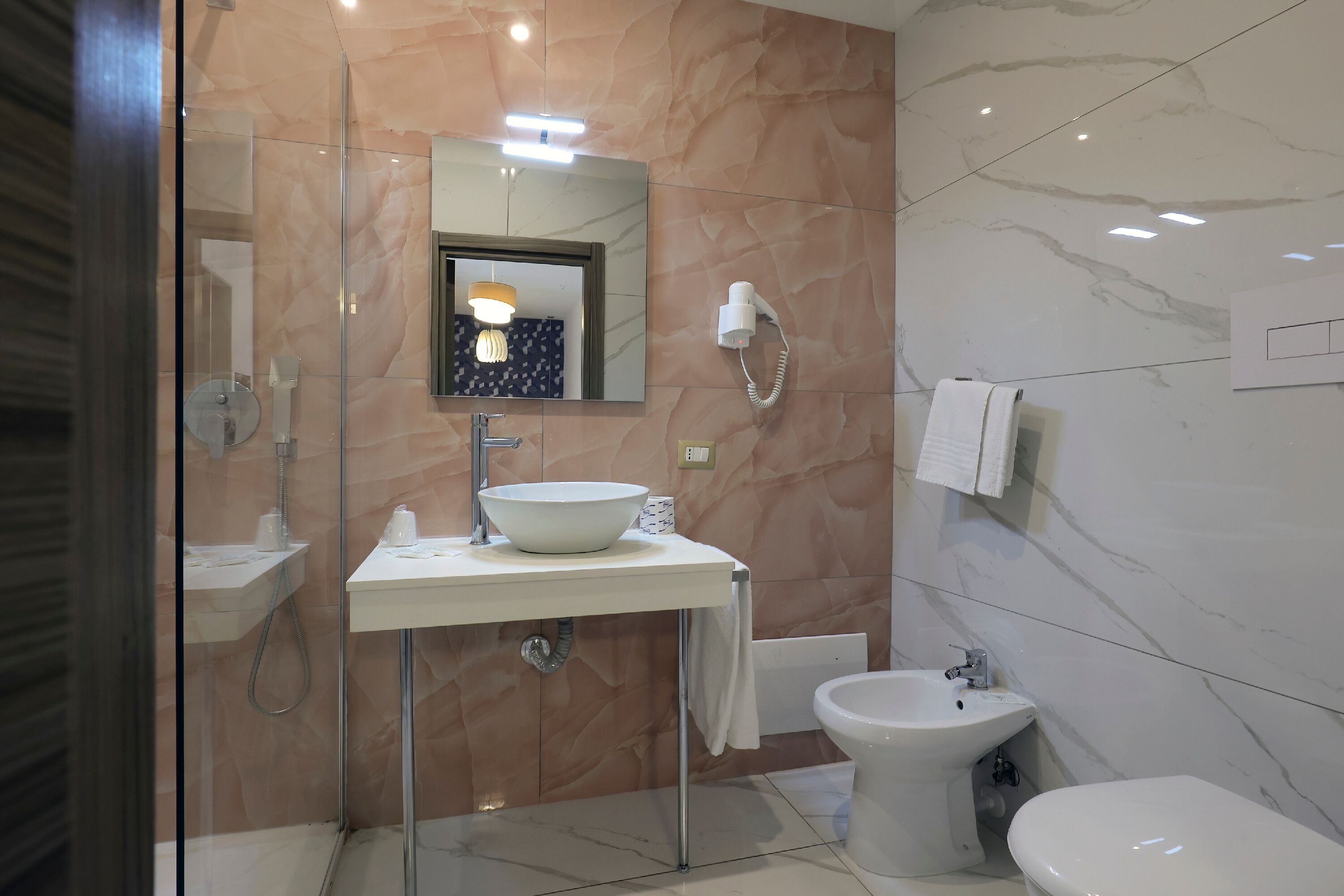 A modern bathroom with a glass-enclosed shower, a white sink with a vessel basin, a mirror, and a bidet.