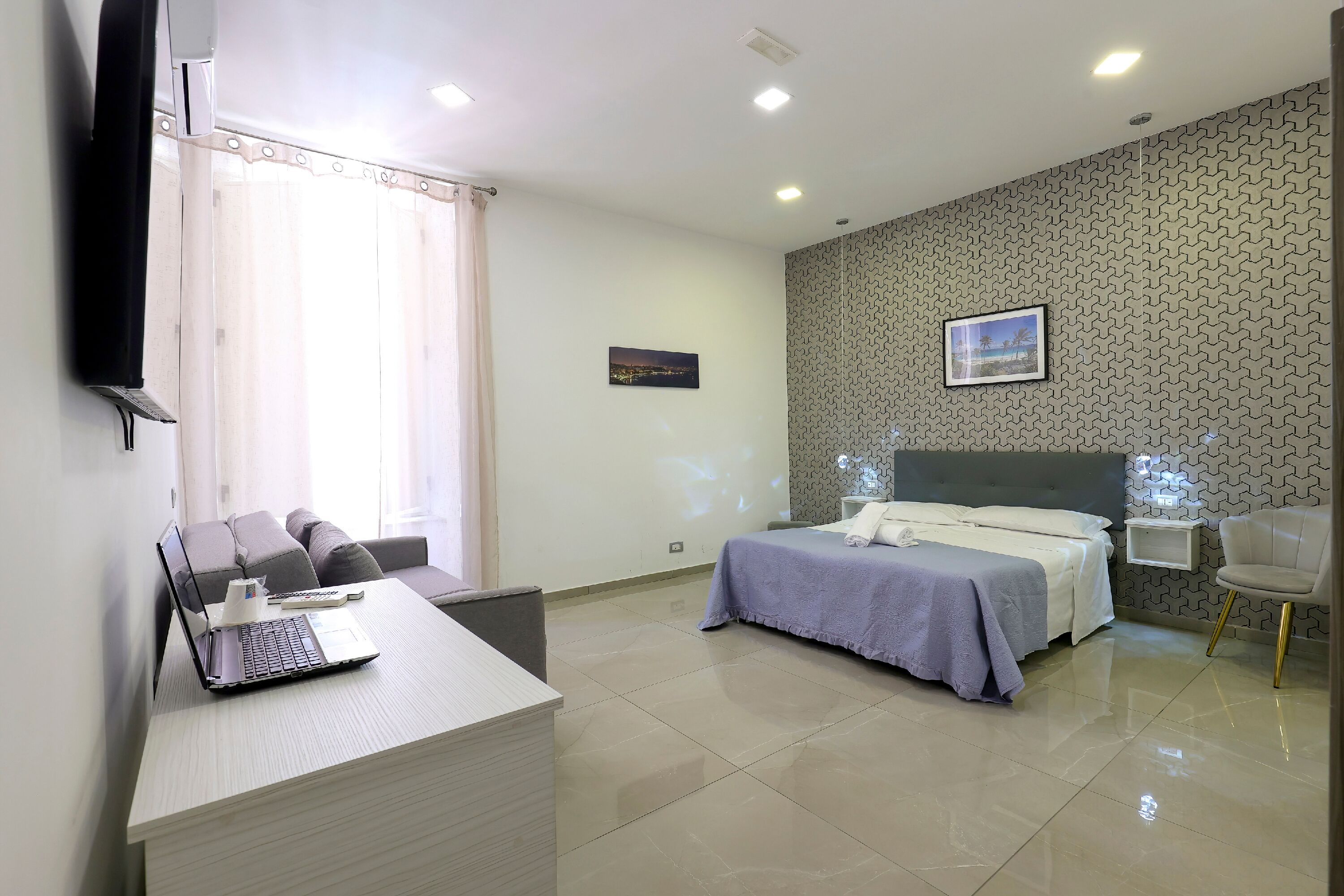 A hotel room with a bed, a desk with a laptop, a chair, and a nightstand.