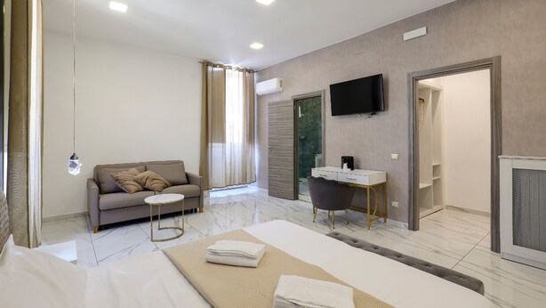 A modern hotel room with a bed, a sofa, a small table, a TV, and a bathroom with a shower and toilet. - Hotel La Pace (Naples)