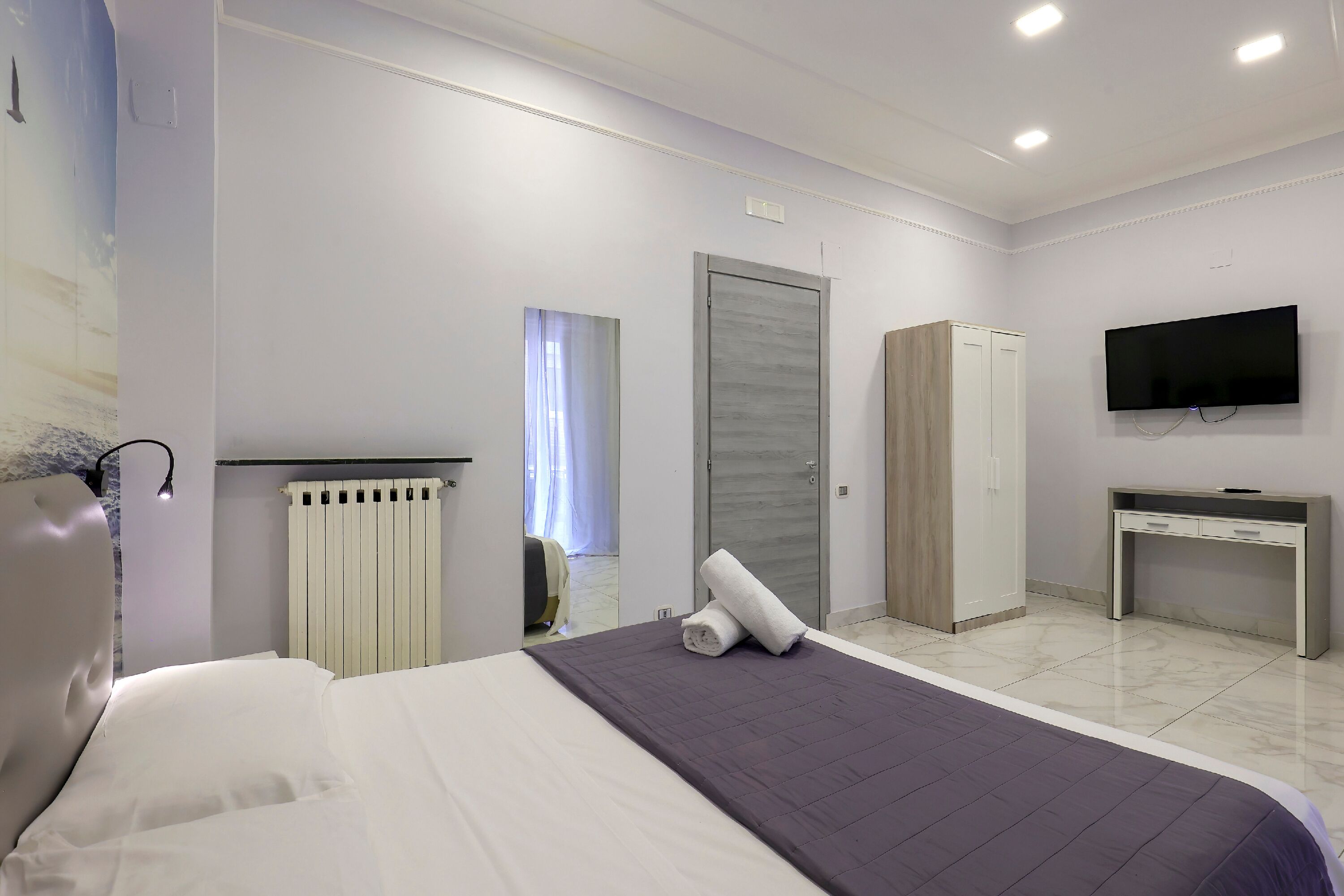 A modern hotel room with a bed, a desk, a wardrobe, and a TV.