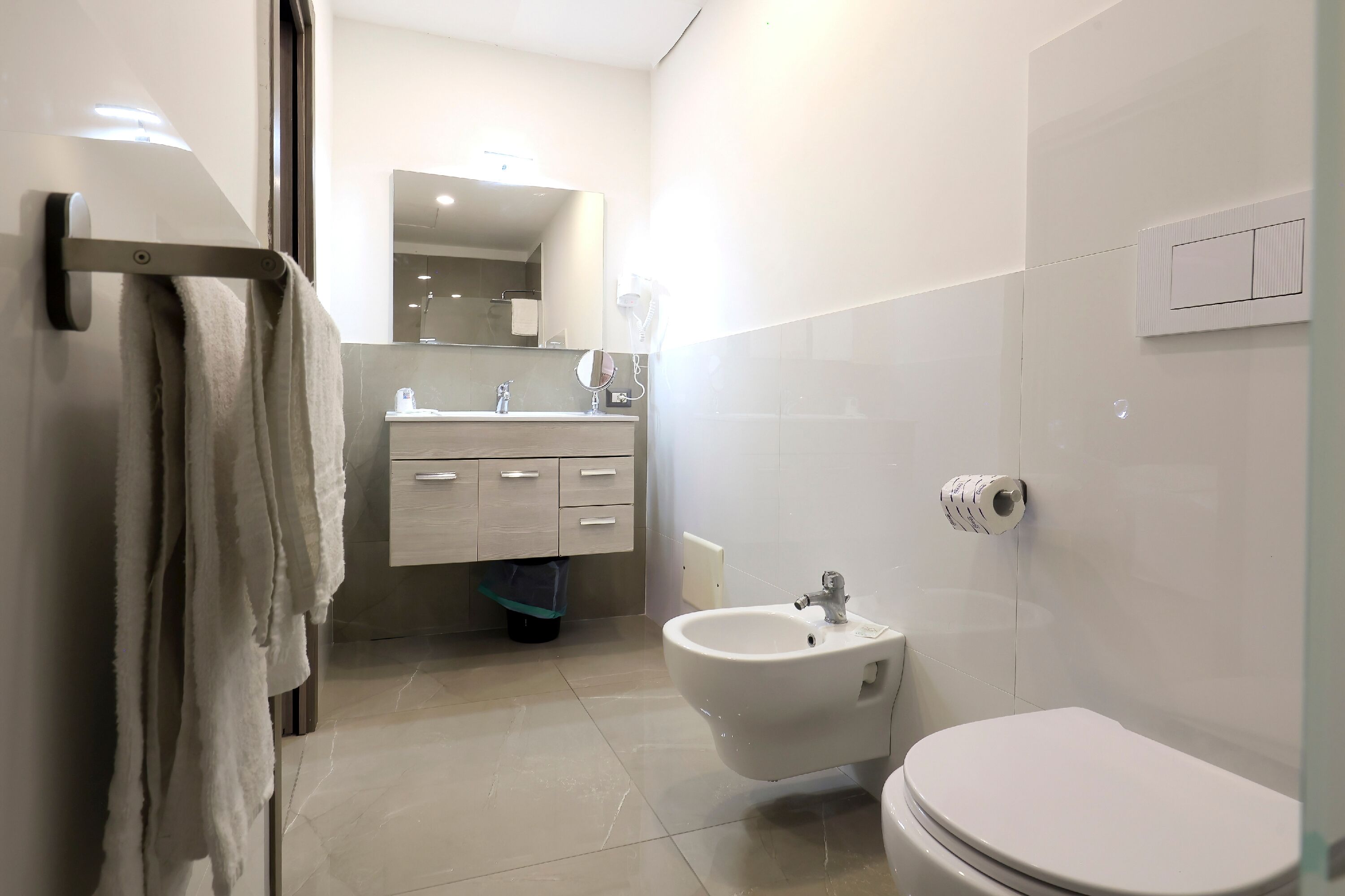 A modern bathroom with a toilet, bidet, sink, and mirror.
