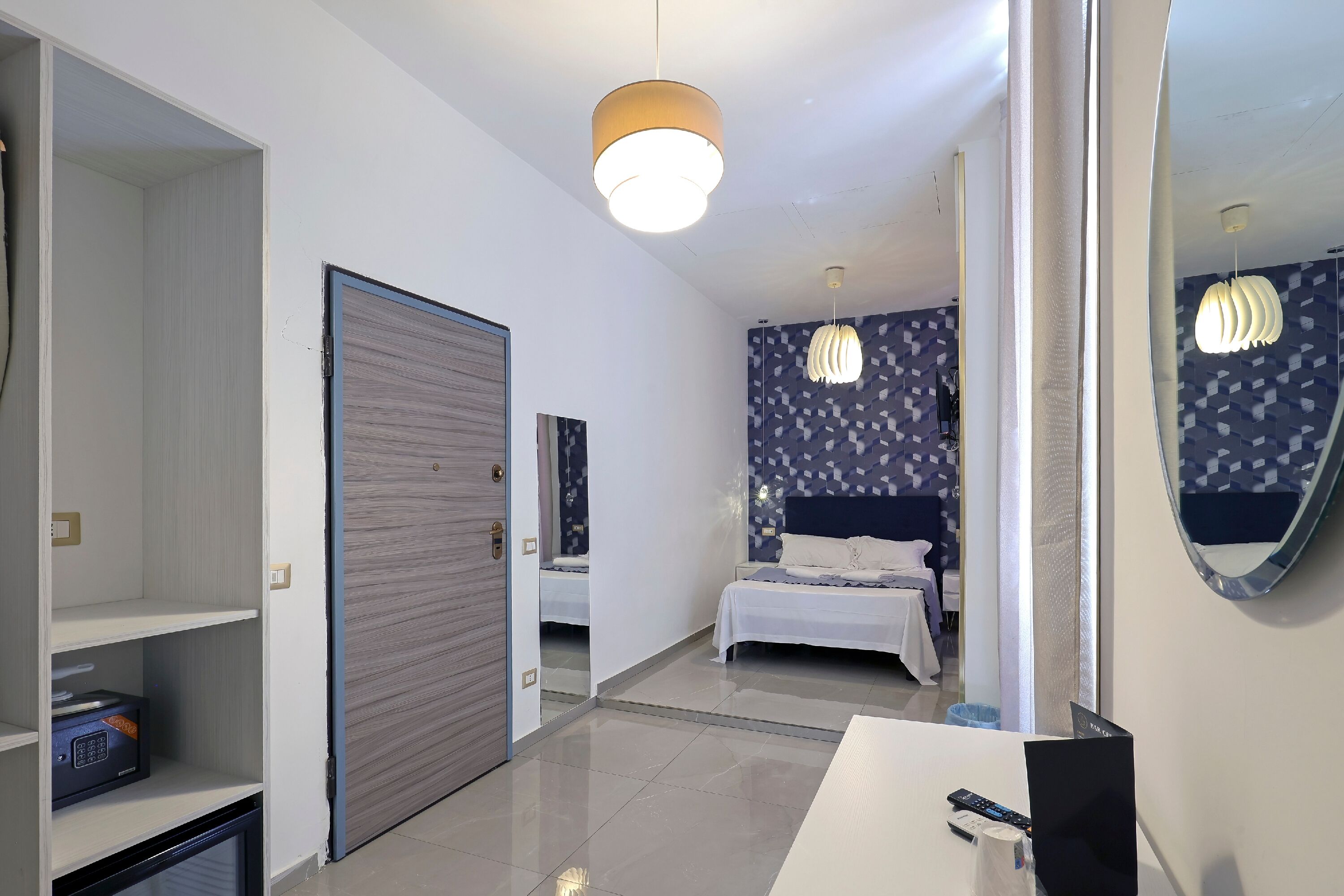 Habitació d'hotel amb llit, taula de nit, mirall, armari i llum al sostre.
