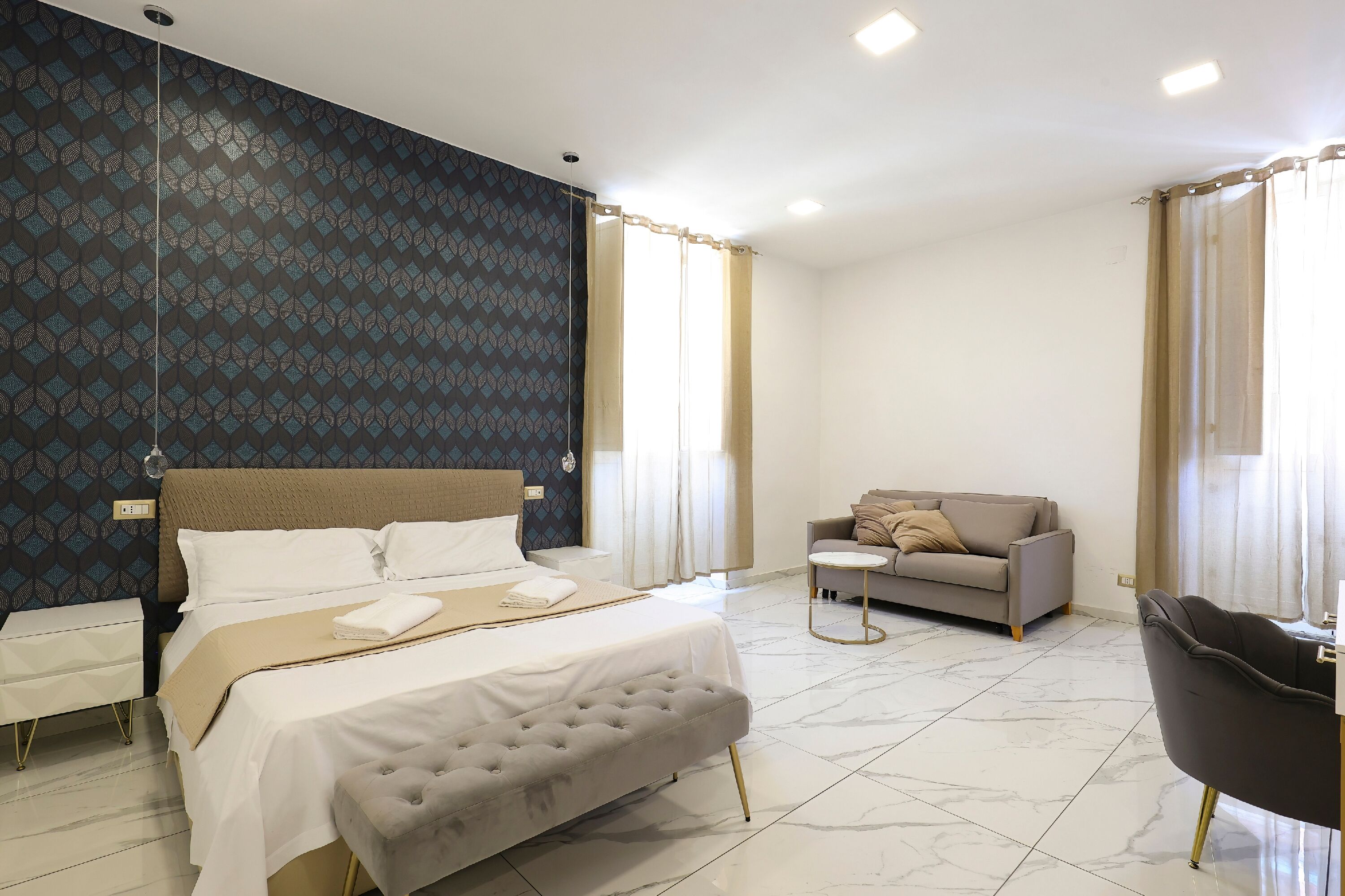 A modern hotel room with a large bed, a sofa, a small table, and a chair.
