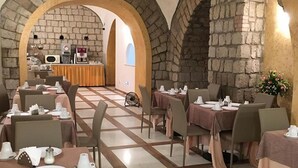 A restaurant with stone walls and arched doorways, tables set with white tableware, and a visible kitchen area. - Hotel La Pace (Naples)