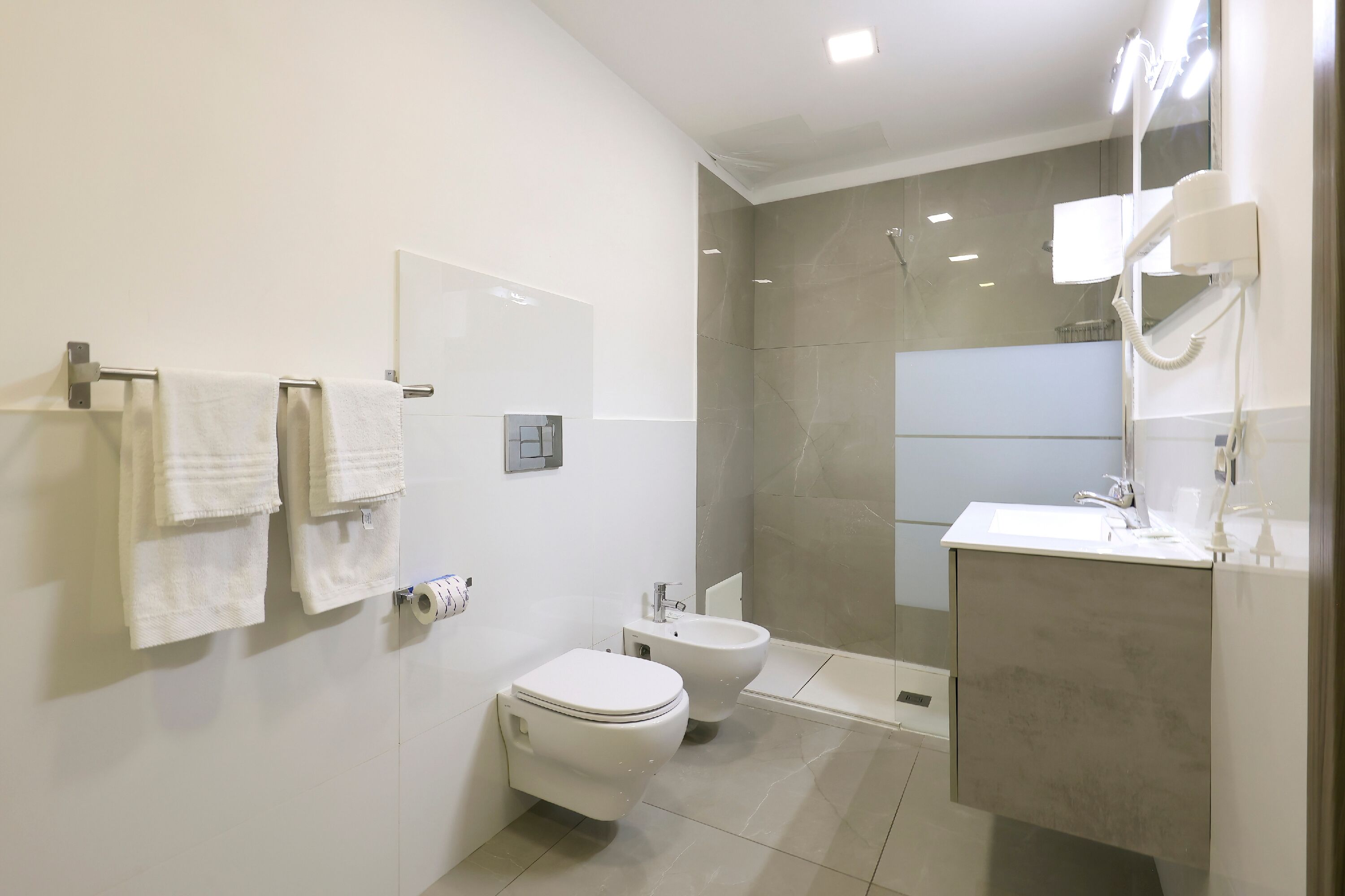 A modern bathroom with a toilet, bidet, and a large mirror.