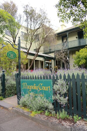 Señal del Bed & Breakfast Magnolia Court, con una cerca de piquetes verdes y plantas de lavanda.