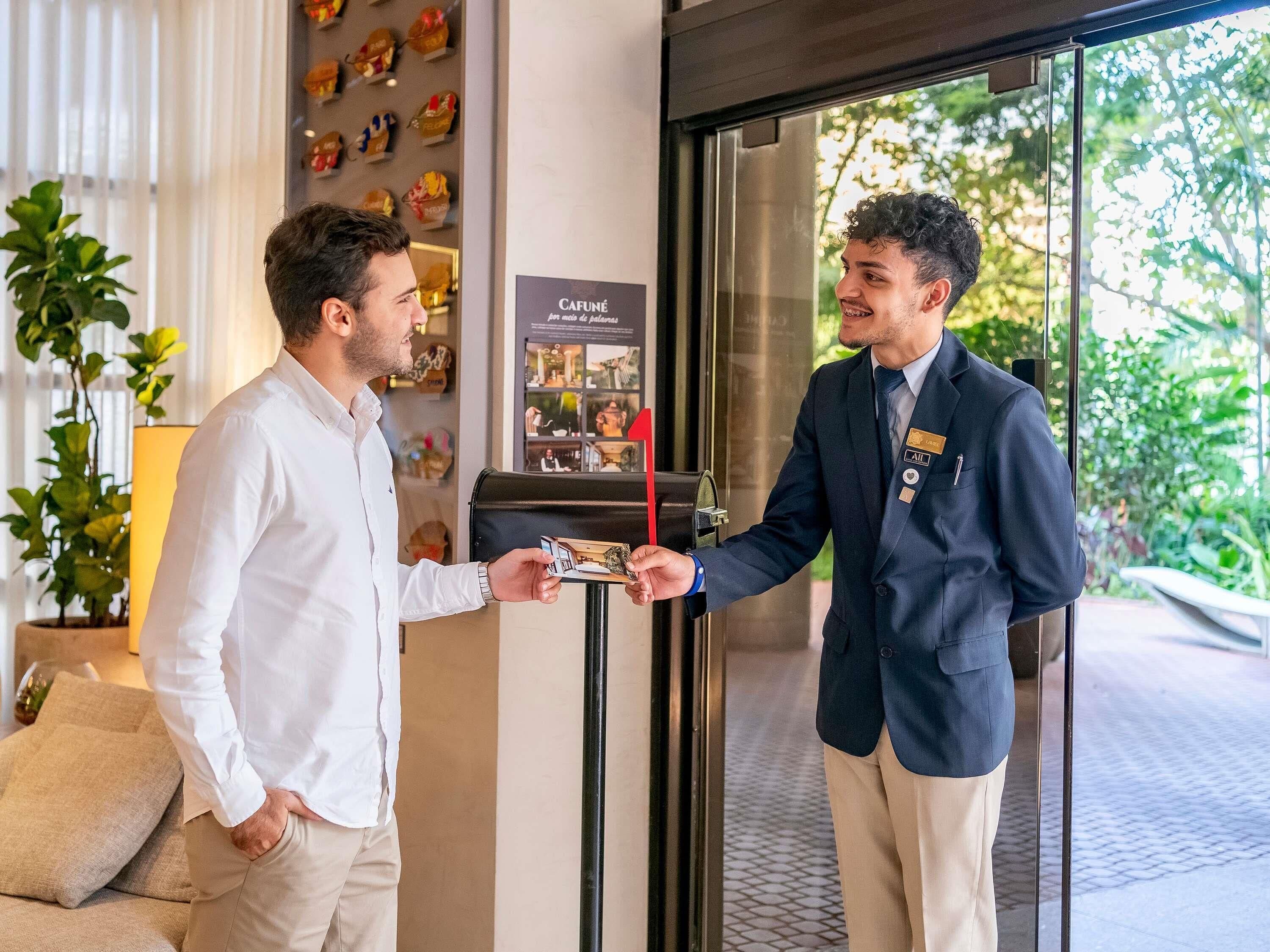 A man handing a key to another man at a hotel entrance.