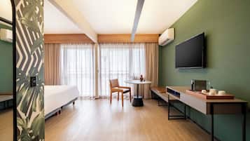 A hotel room with a bed, a round table with chairs, a TV mounted on the wall, and a window with curtains.