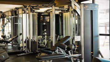 A gym with various exercise machines, including a Smith machine and a cable machine, with a window providing natural light.
