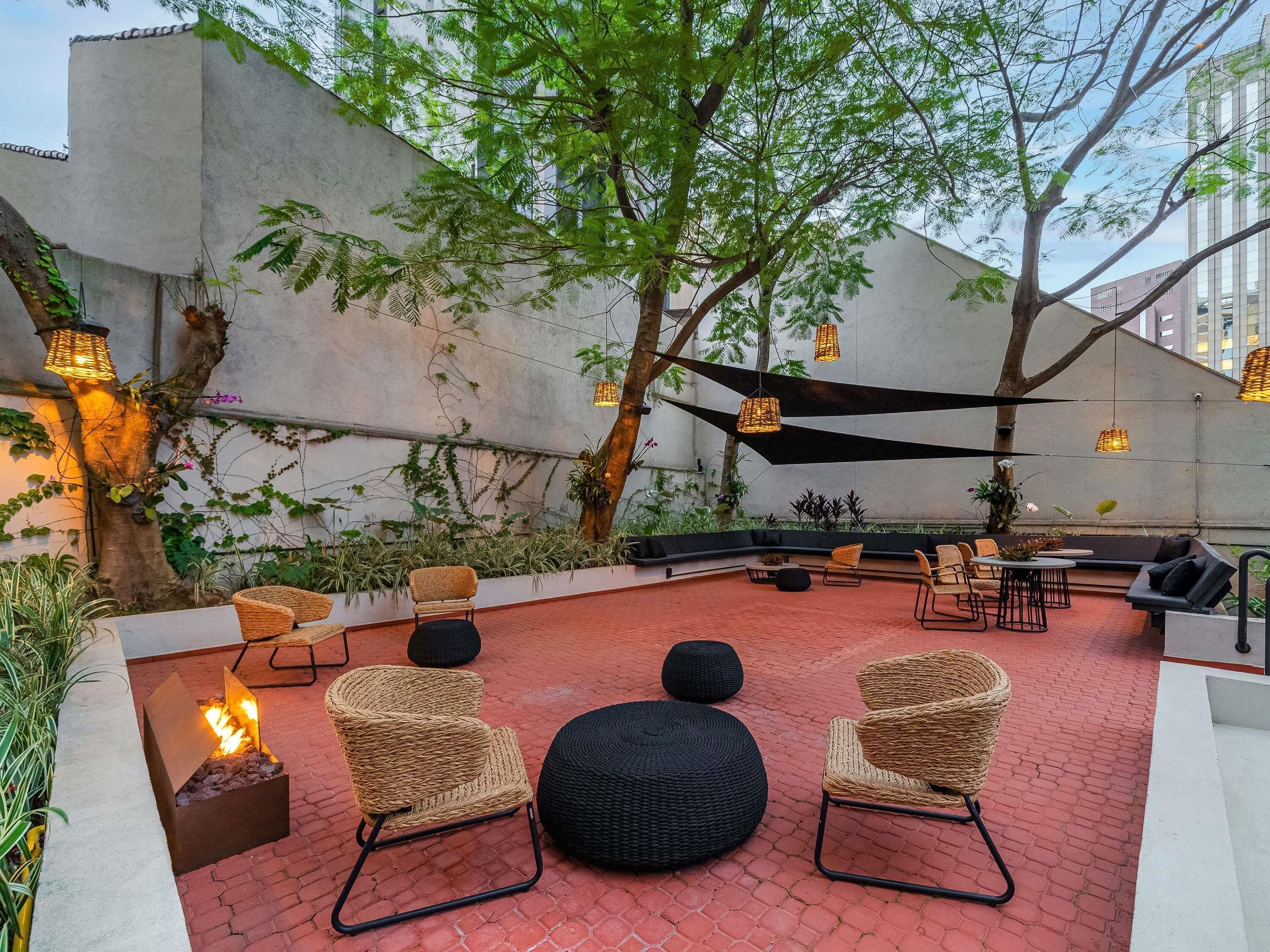 Un espacio al aire libre con mobiliario de mimbre, una chimenea y luces colgantes.