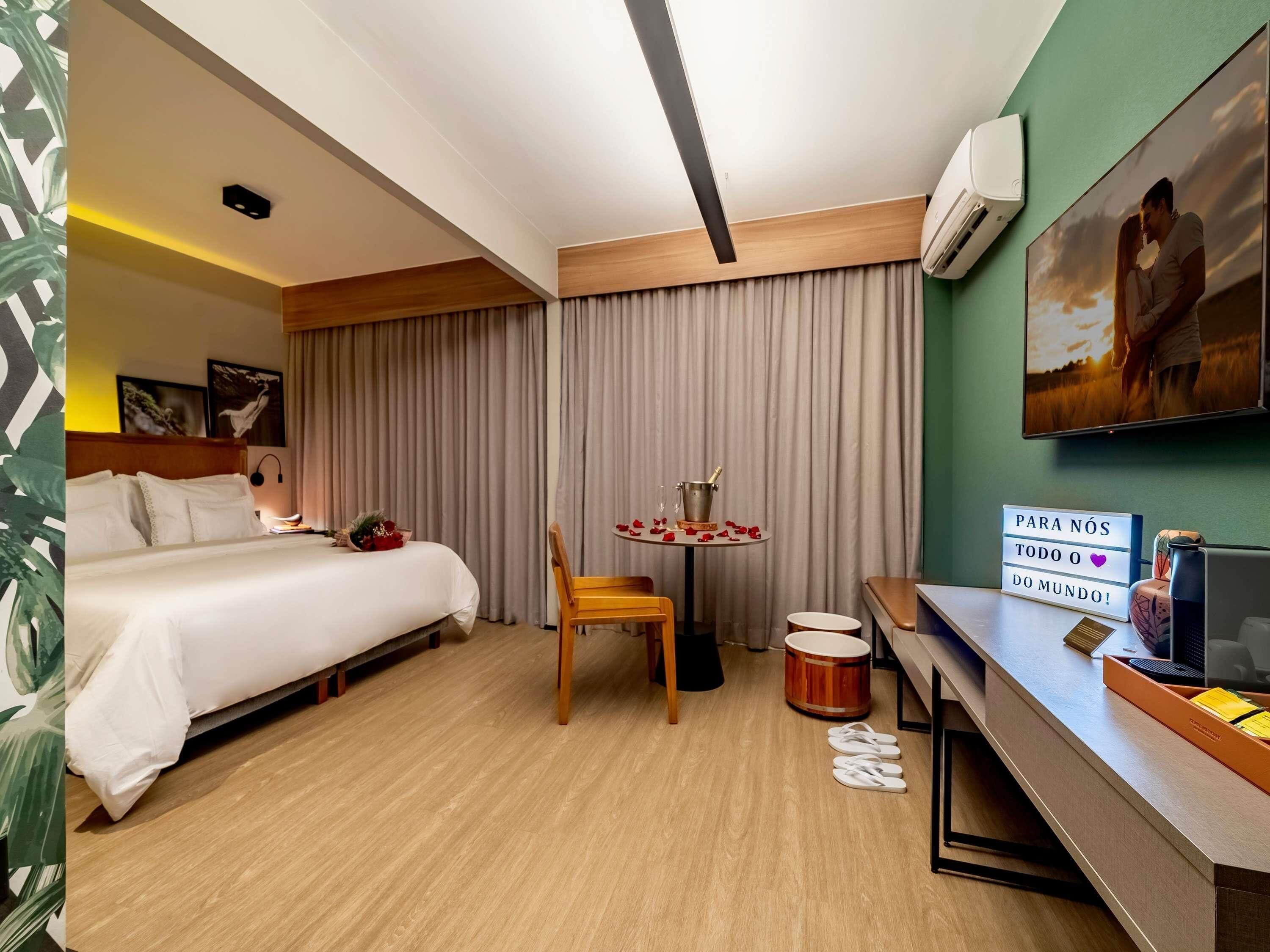 Une chambre d’hôtel avec un lit, un bureau, une chaise, une table avec une boisson et un tableau au mur.