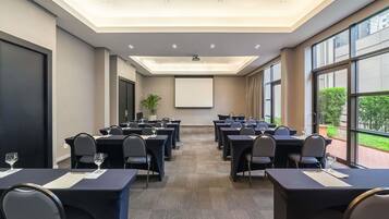 A conference room with tables, chairs, a projector screen, and large windows.