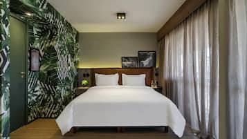 A hotel room with a large bed, a nightstand, a wall clock, and a window with curtains.