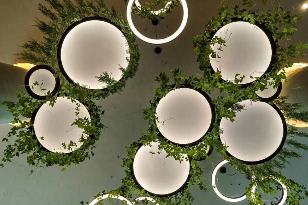 A ceiling with circular light fixtures surrounded by greenery.