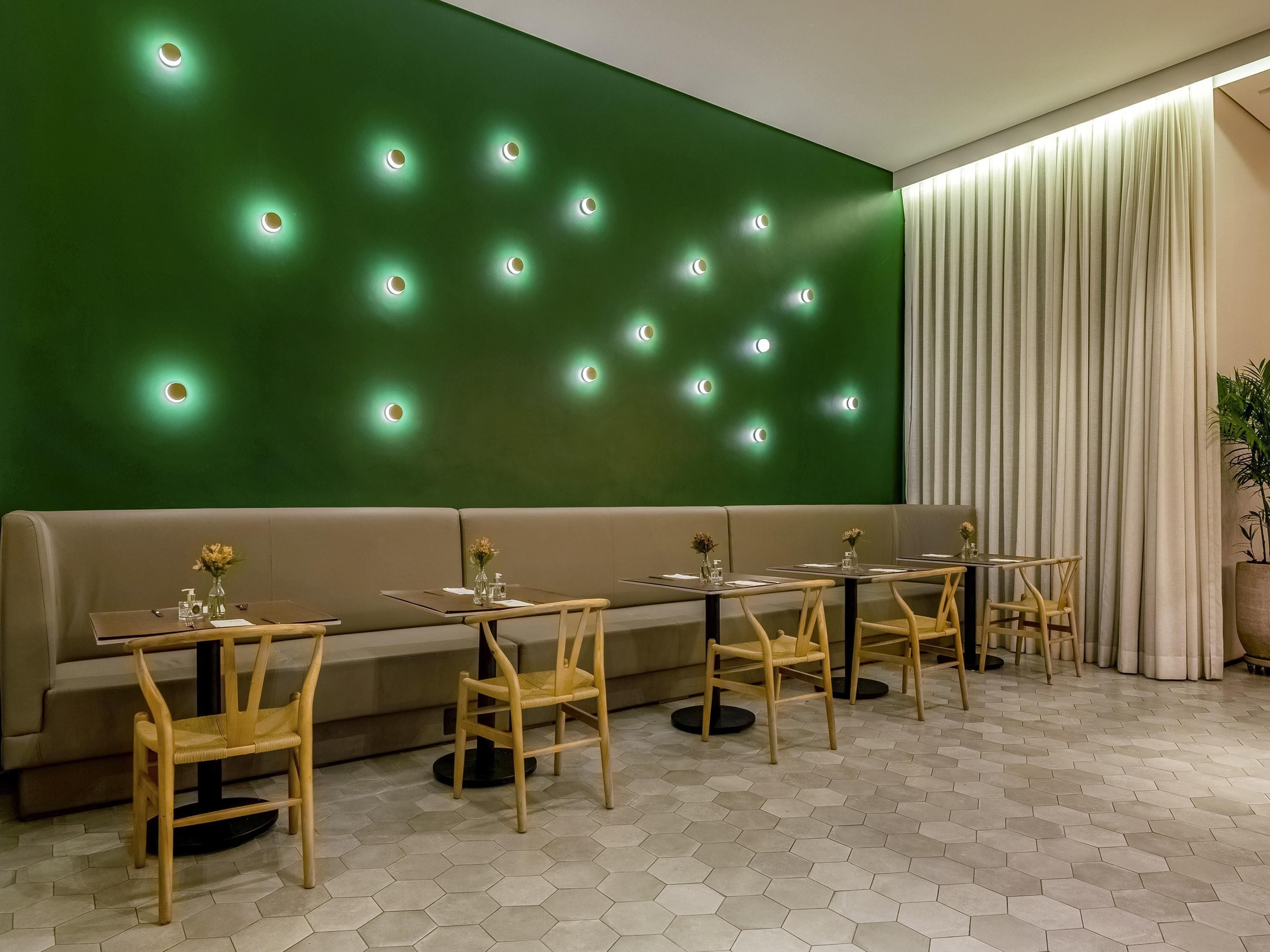 A restaurant with a green wall, hexagonal floor tiles, wooden chairs, and tables.