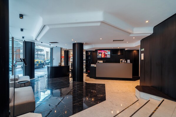 A modern lobby with a reception desk, seating area, and glass doors leading outside.