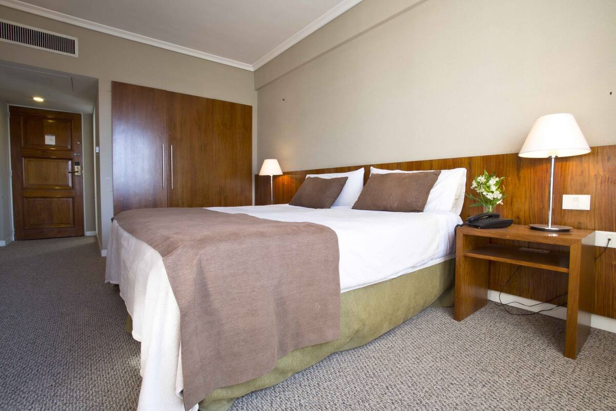 Ein Hotelzimmer mit einem großen Bett, zwei Nachttischen mit Lampen, einem Holzschrank und einem Teppichboden.