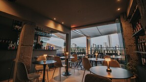A modern bar with round tables and chairs, a high bar counter, and a view of the city skyline through large windows. - Bisonte Libertad (Buenos Aires)