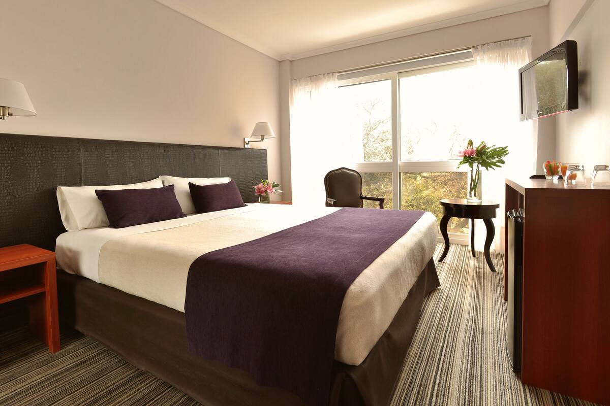 Ein Hotelzimmer mit einem großen Bett, einem Schreibtisch, einem Sessel und einem an der Wand befestigten Fernseher.