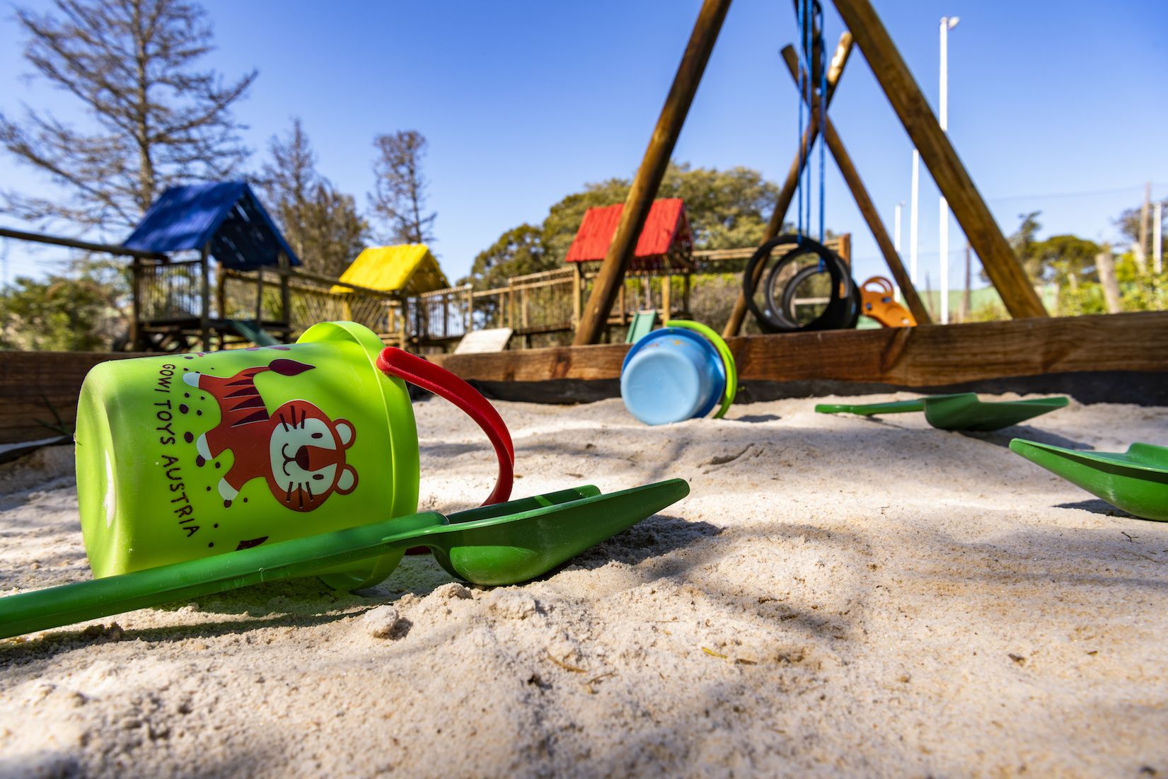 A sandy area with a green bucket labeled 'GOWI TOYS AUSTRIA' and a blue container.