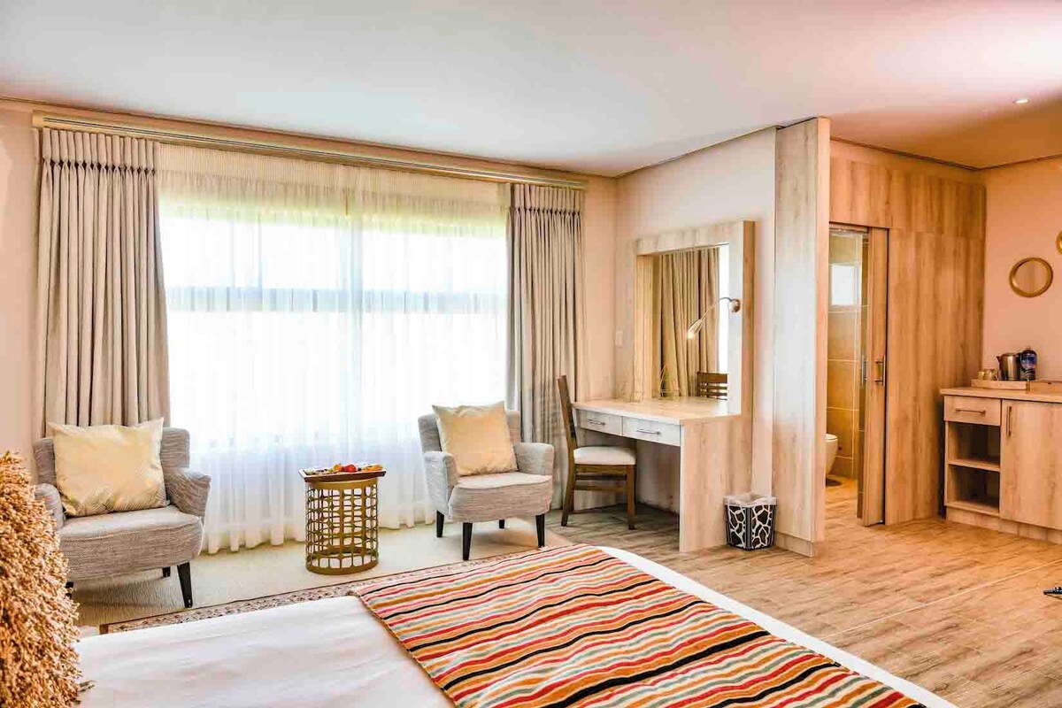 A hotel room with a bed, two armchairs, a desk, and a mirror.