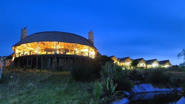 A large, circular building with a wooden exterior and multiple chimneys, surrounded by smaller houses with similar architecture. - Kwantu Private Game Reserve (Sidbury)