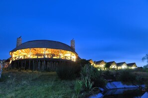 Um edifício grande e circular, com fachada de madeira e várias chaminés, rodeado por casas menores com arquitetura semelhante.