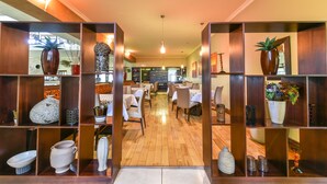 A spacious hotel lobby with wooden shelving displaying various decorative items, a central seating area with tables and chairs, and a warm, inviting atmosphere. - Kwantu Private Game Reserve (Sidbury)