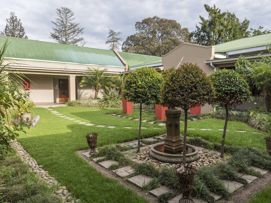 Un giardino curato con un vialetto in pietra, una fontana al centro e un edificio con tetto verde.
