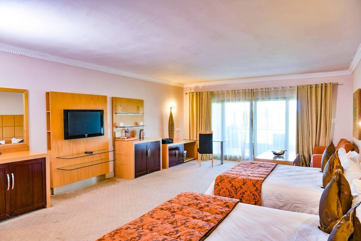 Une chambre d’hôtel équipée d’une télévision, de meubles en bois, d’un bureau, d’une chaise, d’un lit avec une couvre-lit à motifs et d’une fenêtre avec des rideaux.