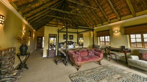 A spacious room with a high ceiling, a large bed, a red sofa, and a dining area with a table and chairs. - Kwantu Private Game Reserve (Sidbury)