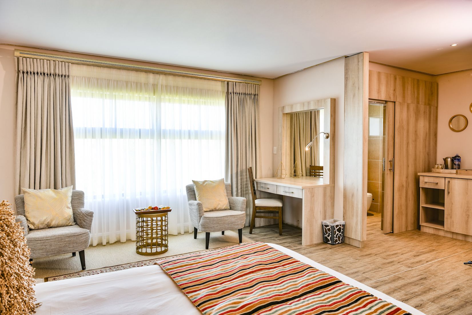 A hotel room with a bed, two armchairs, a desk, and a mirror.