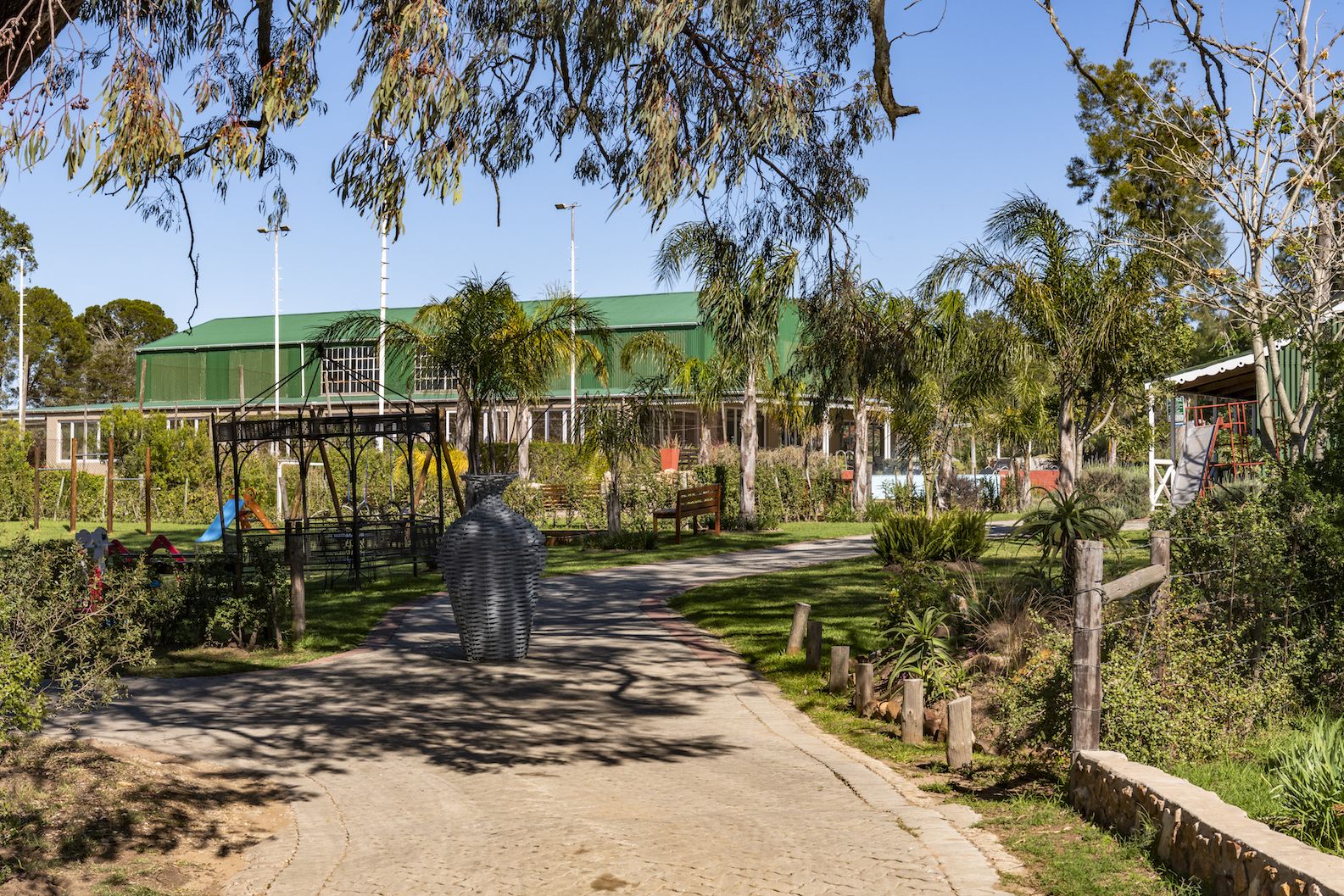 A pathway leading to a building with a green roof, surrounded by trees and a large sculpture.