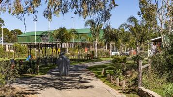 A pathway leading to a building with a green roof, surrounded by trees and a large sculpture.