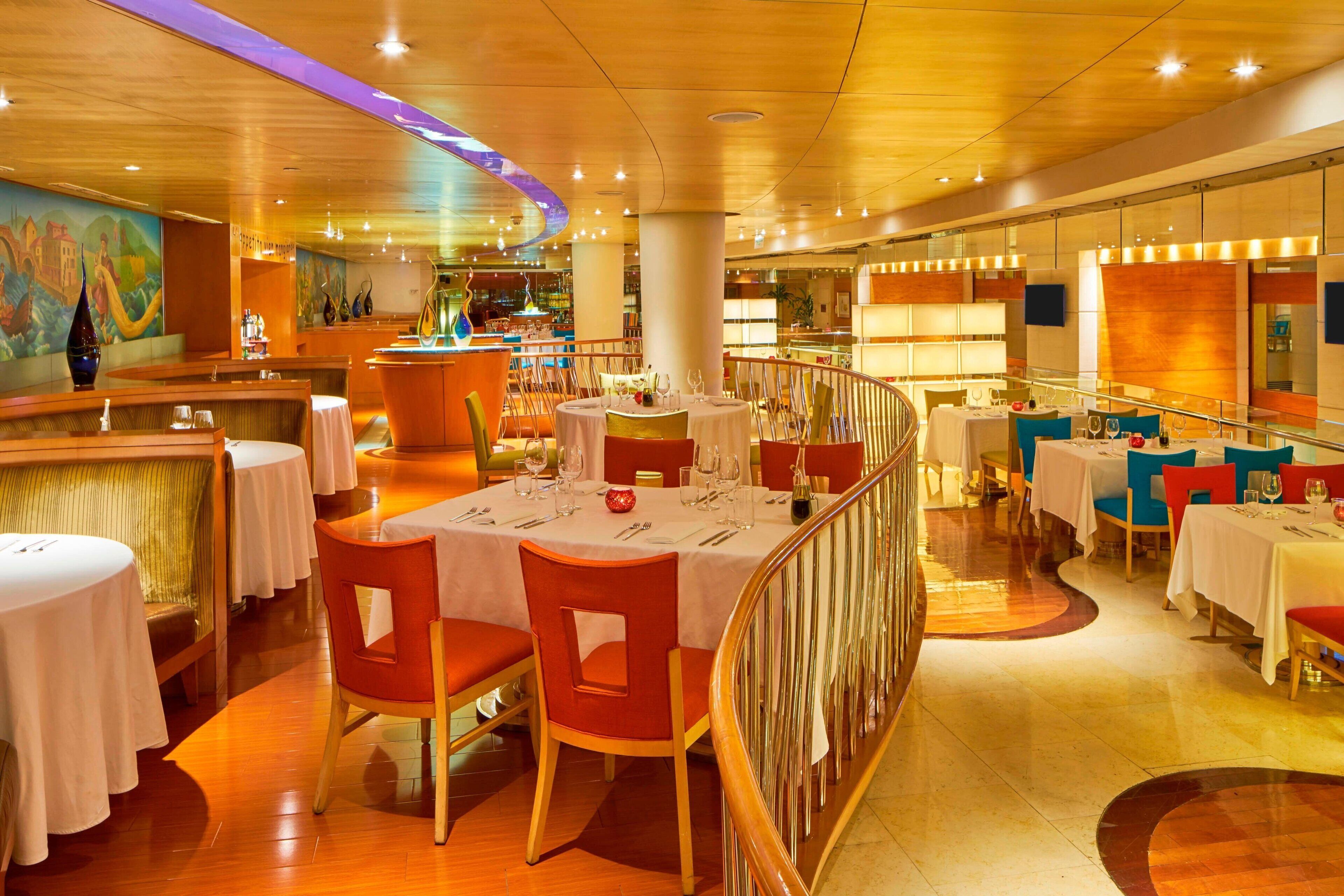 A restaurant with round tables, red chairs, and a bar area.