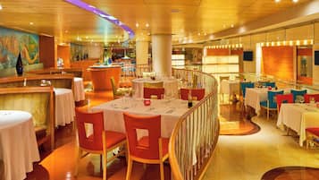 A restaurant with round tables, red chairs, and a bar area.