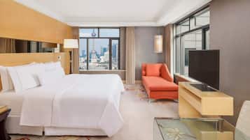 A hotel room with a bed, a TV, a desk, and a view of a cityscape.