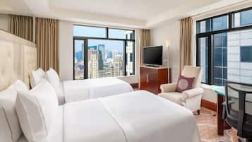 Une chambre d’hôtel avec deux lits, un bureau, une chaise, une télévision et une vue sur la ville.