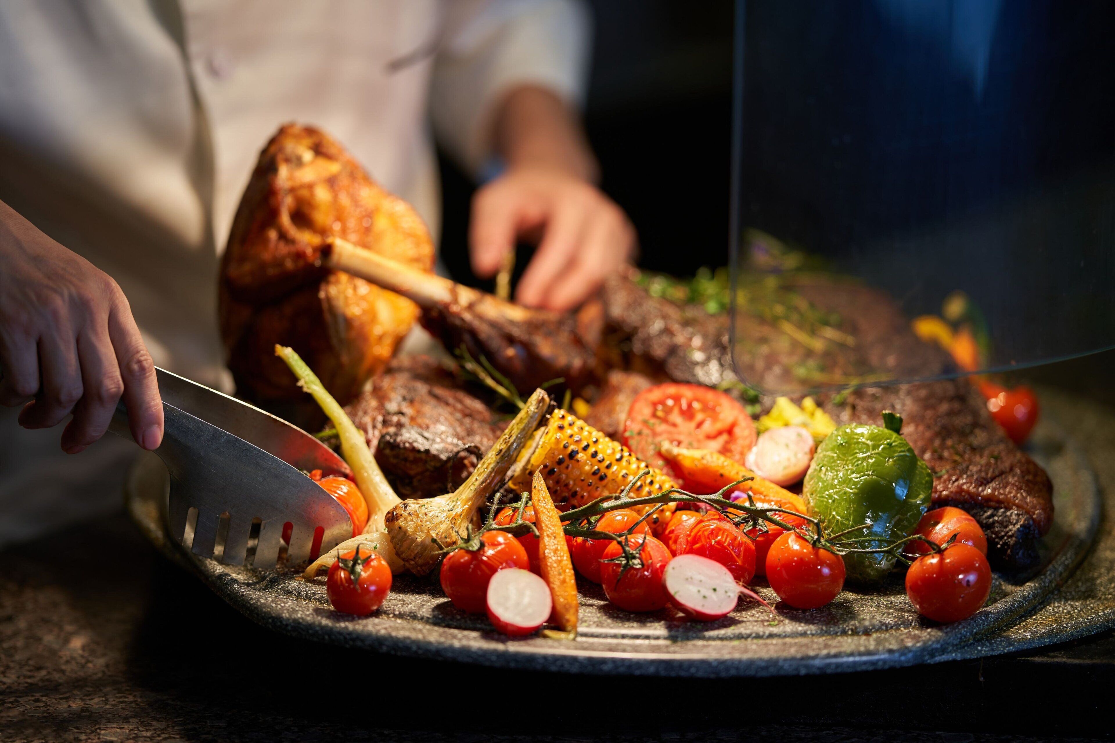 A chef carving a roasted chicken with vegetables on a plate.