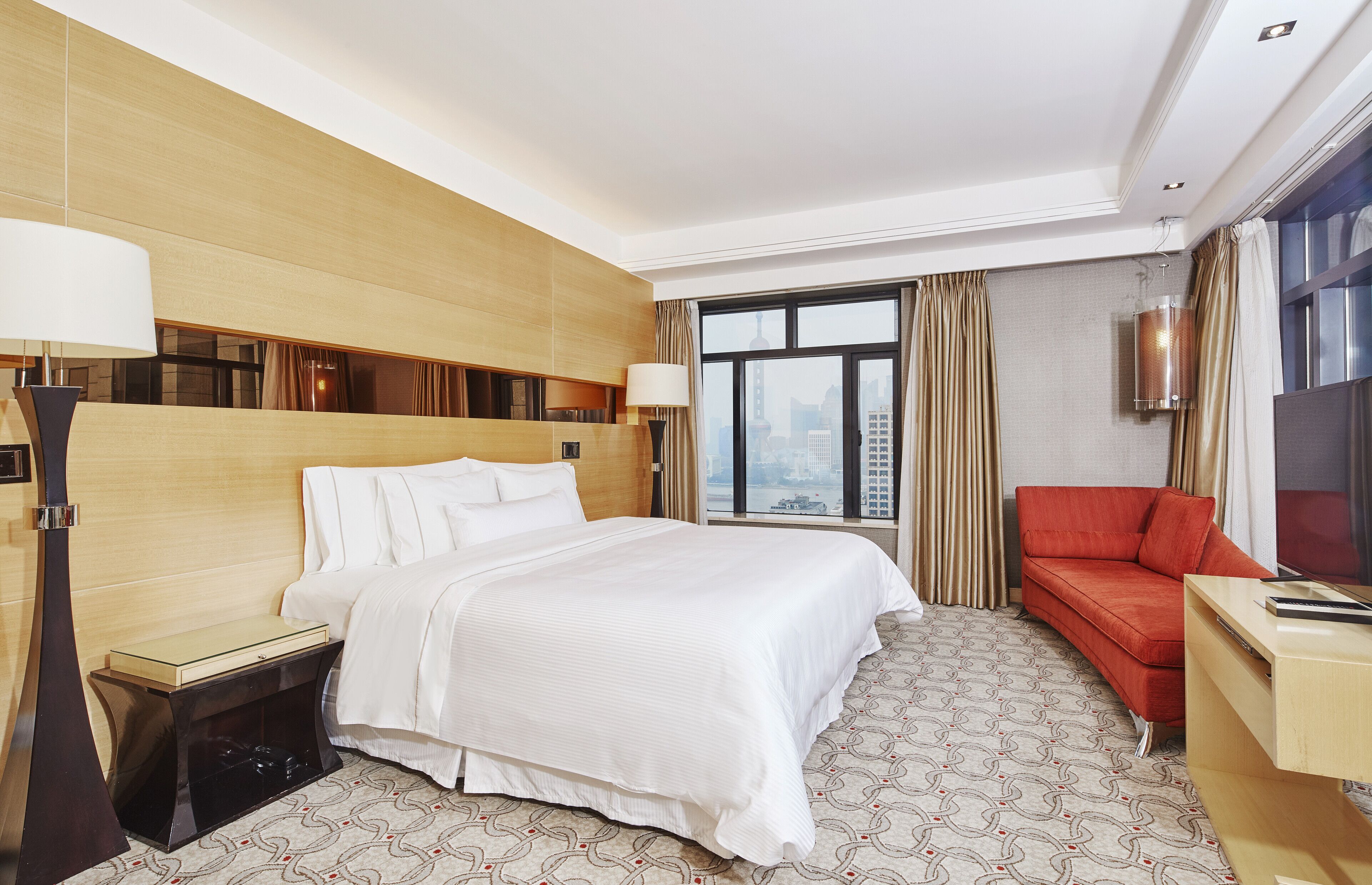 Une chambre d’hôtel avec un grand lit, un canapé rouge, un bureau et une vue sur la ville par la fenêtre.