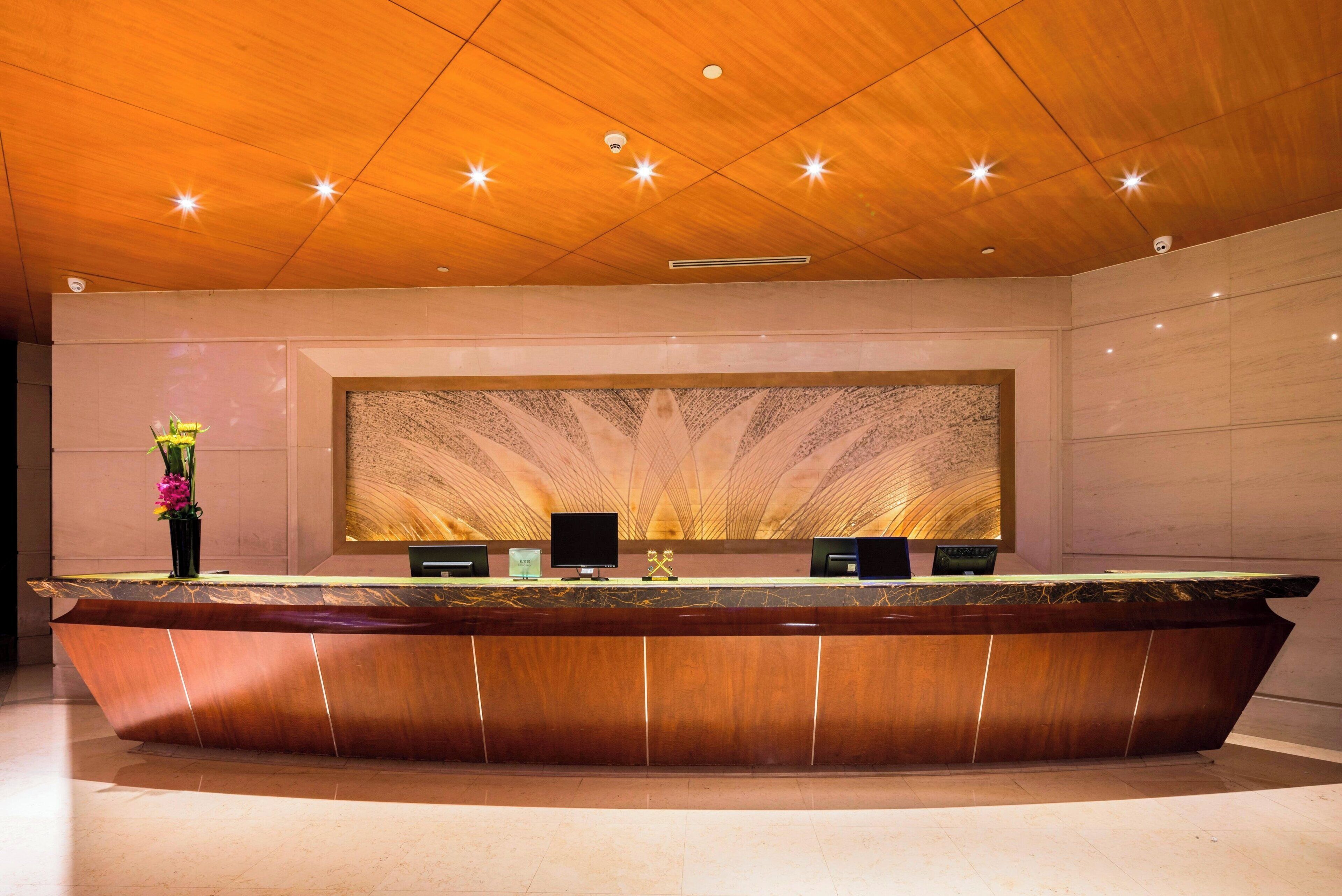 A reception desk with a modern design, a large wall art piece, and a ceiling with recessed lighting.