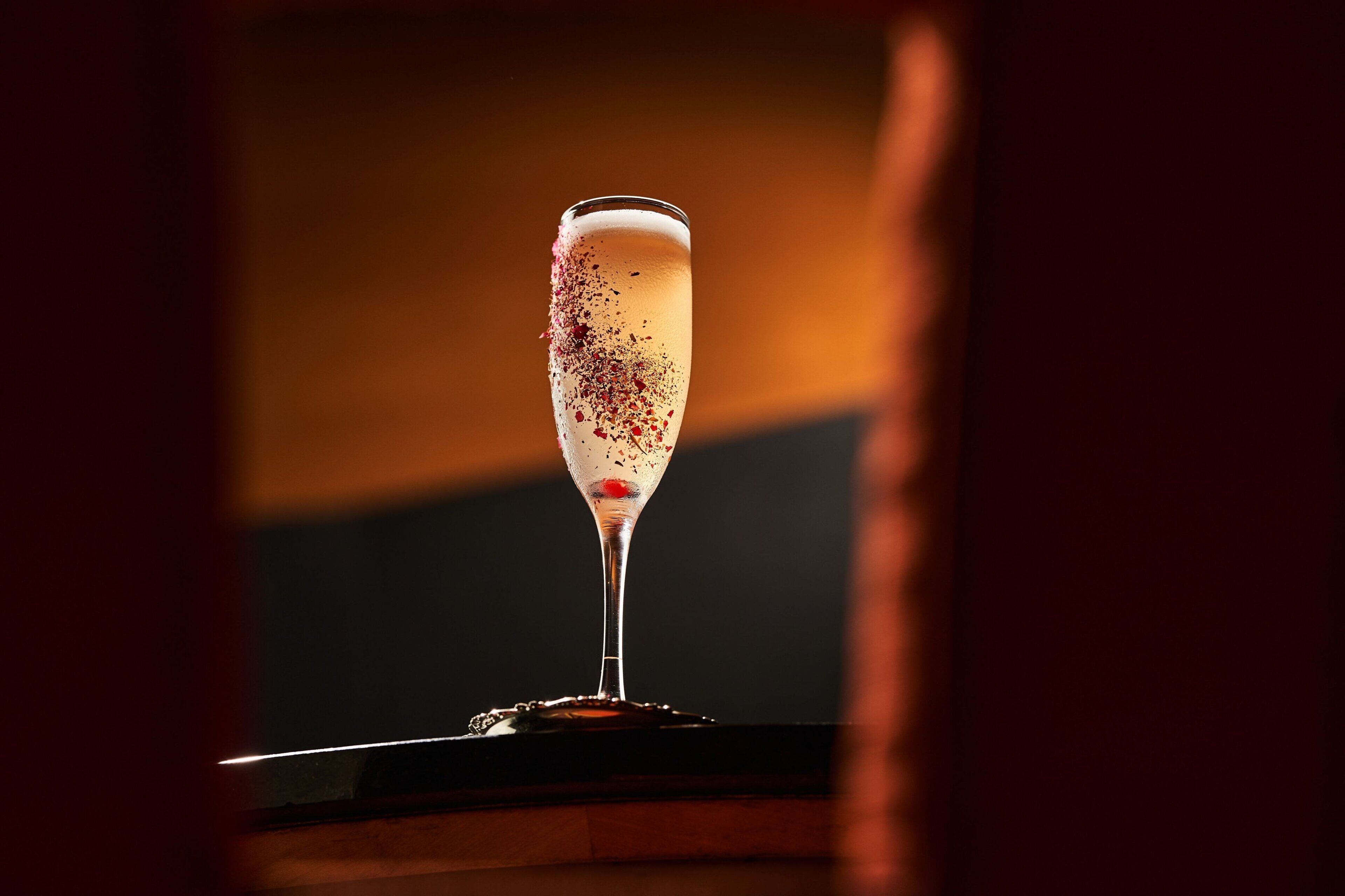 A champagne glass with a frothy top, placed on a reflective surface.